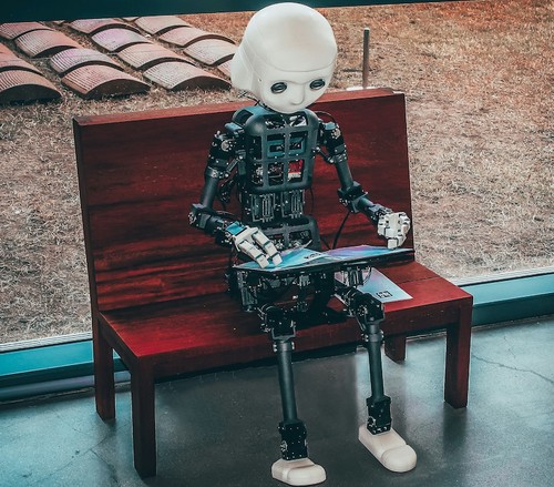 Image of a humanoid robot sitting on a bench, reading a book