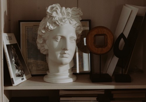 Image of a shelf featuring books and a bust of the head of Apollo