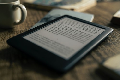Image of an e-reader featuring text on the screen, sitting on a table next to a mug